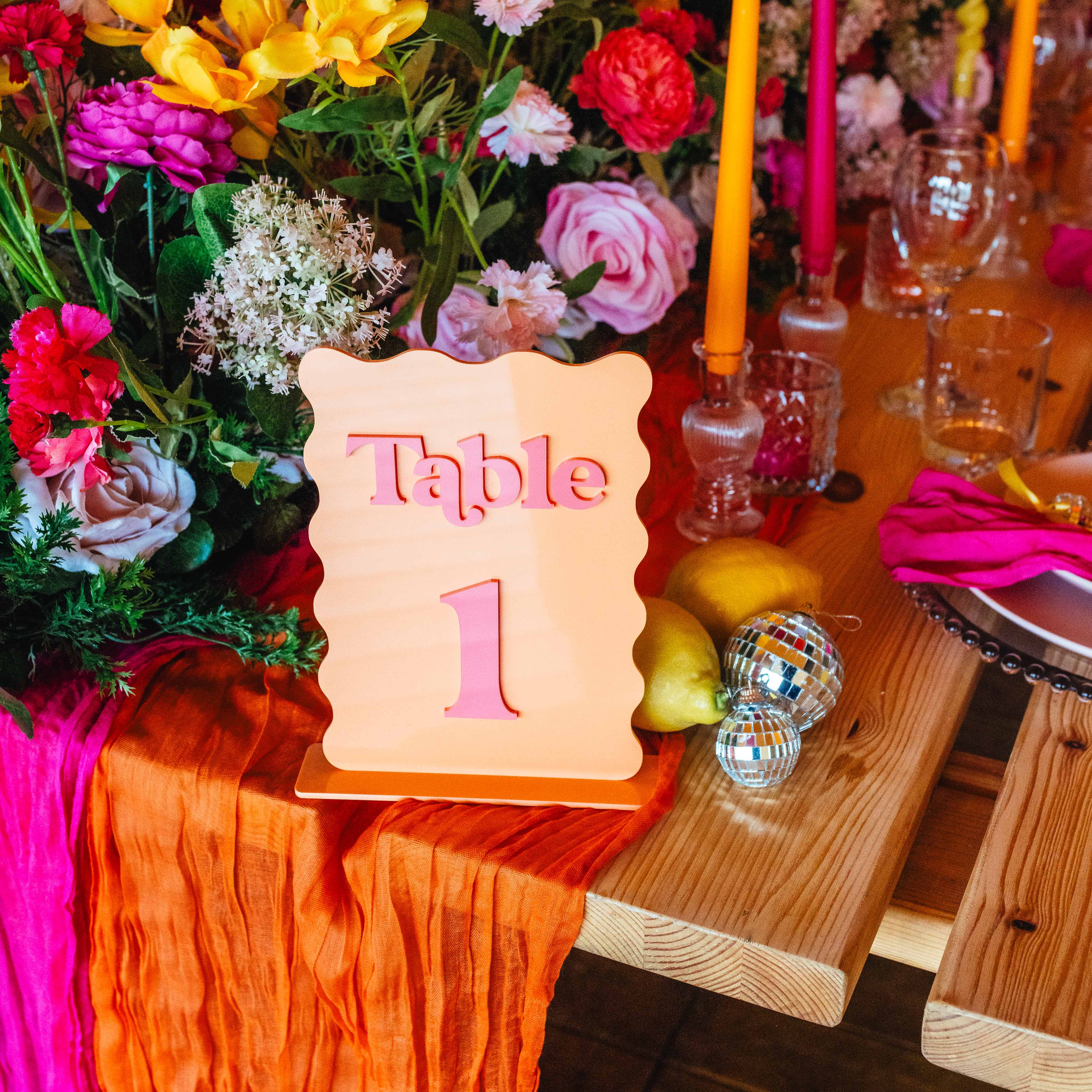 Decorative table setup with flowers, candles, and a table number sign on a wooden table.