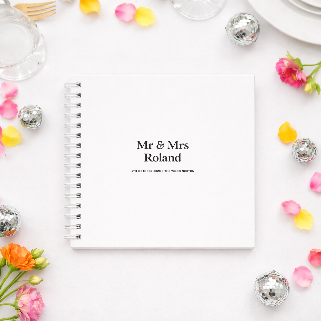 Guestbook with 'Mr & Mrs Roland' on a white surface with decorative flowers and objects.