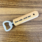 Wooden bottle opener with 'Save water, drink beer' text on a wooden surface