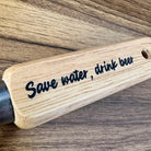 Wooden handle with 'Save water, drink beer' engraving on a wooden background