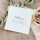 White card with 'Will you be my Maid of Honour?' text on a textured surface with flowers.