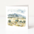 Greeting card with a scenic landscape featuring mountains, trees, and sheep on a white background.