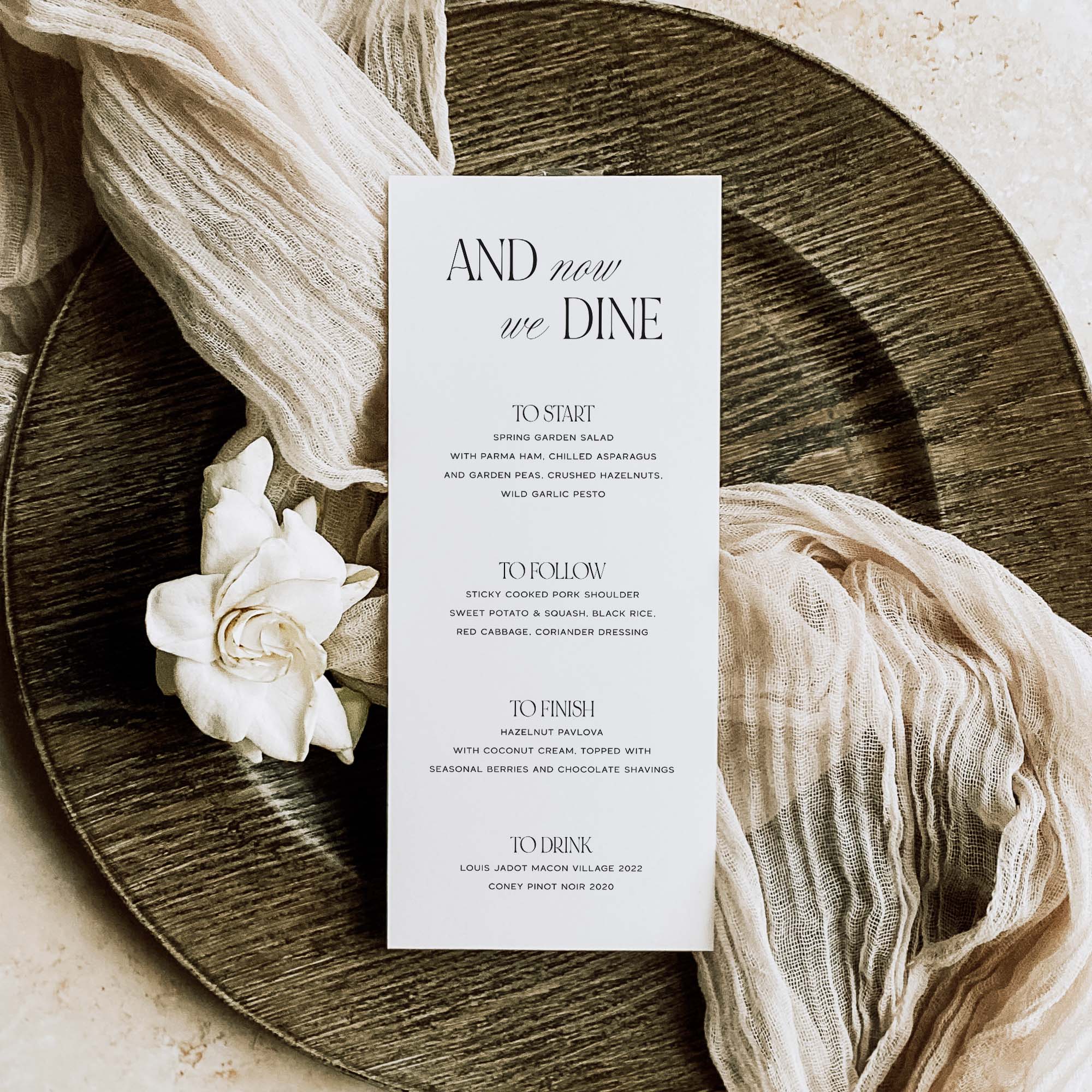 Wedding breakfast menu on a wooden plate with a white flower and fabric