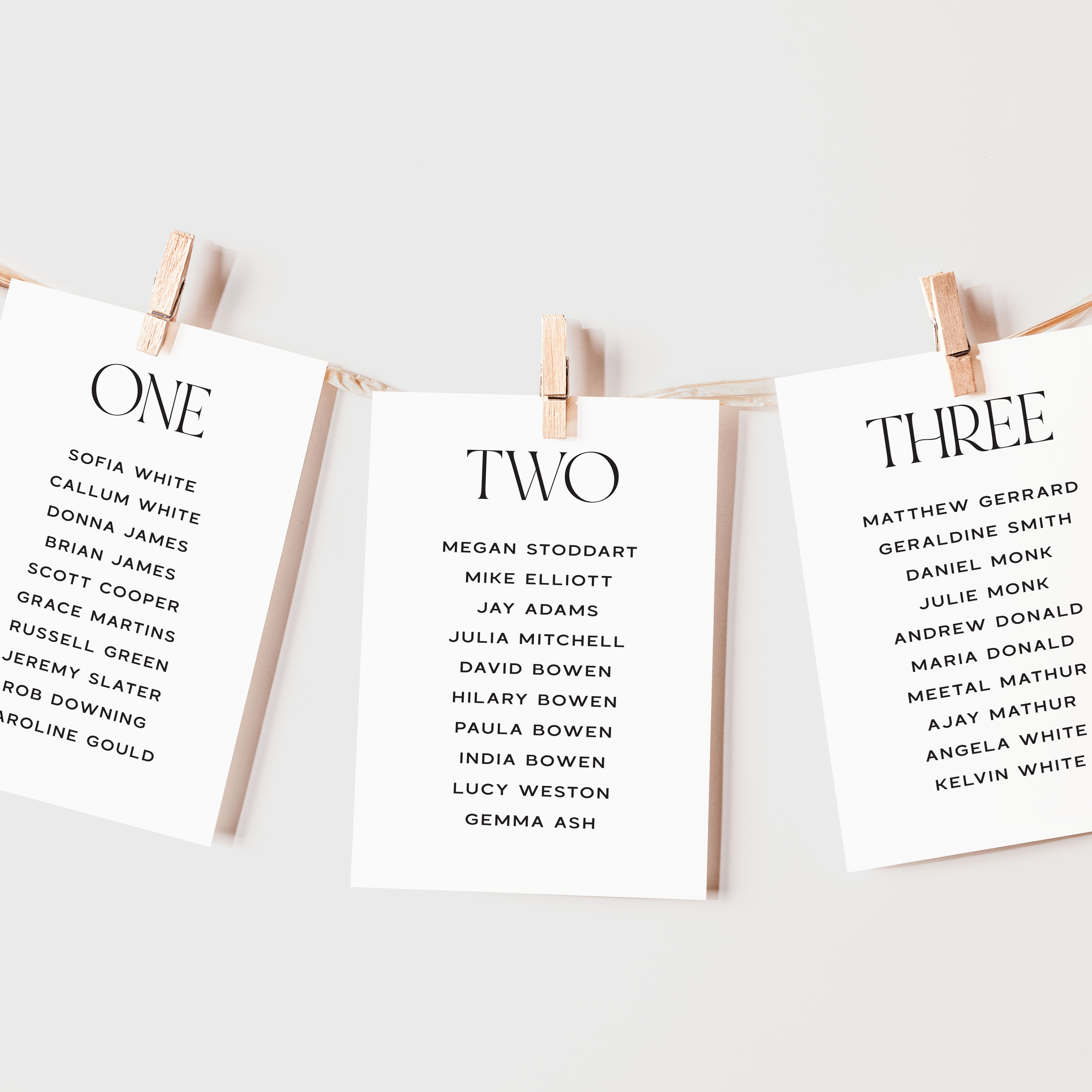 Wedding table plan cards with names on them, each labeled 'ONE', 'TWO', and 'THREE', hanging on a line with wooden clips.