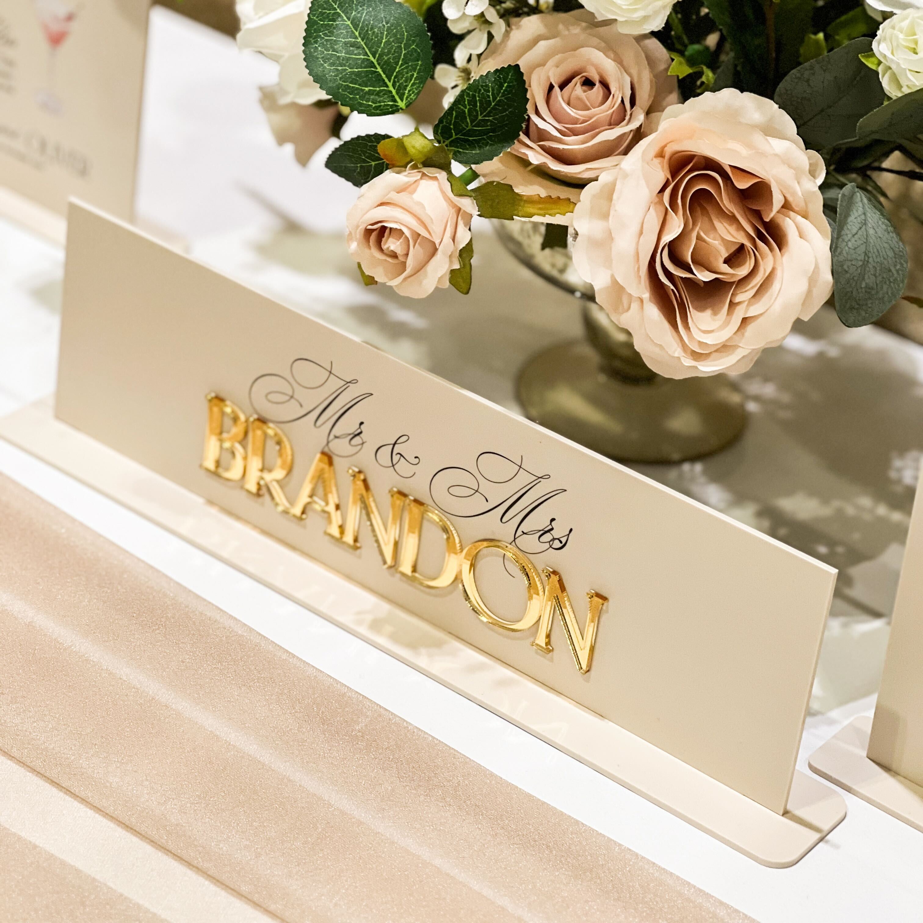 Floral arrangement with a decorative sign reading 'Mr & Mrs Brandon' on a table.