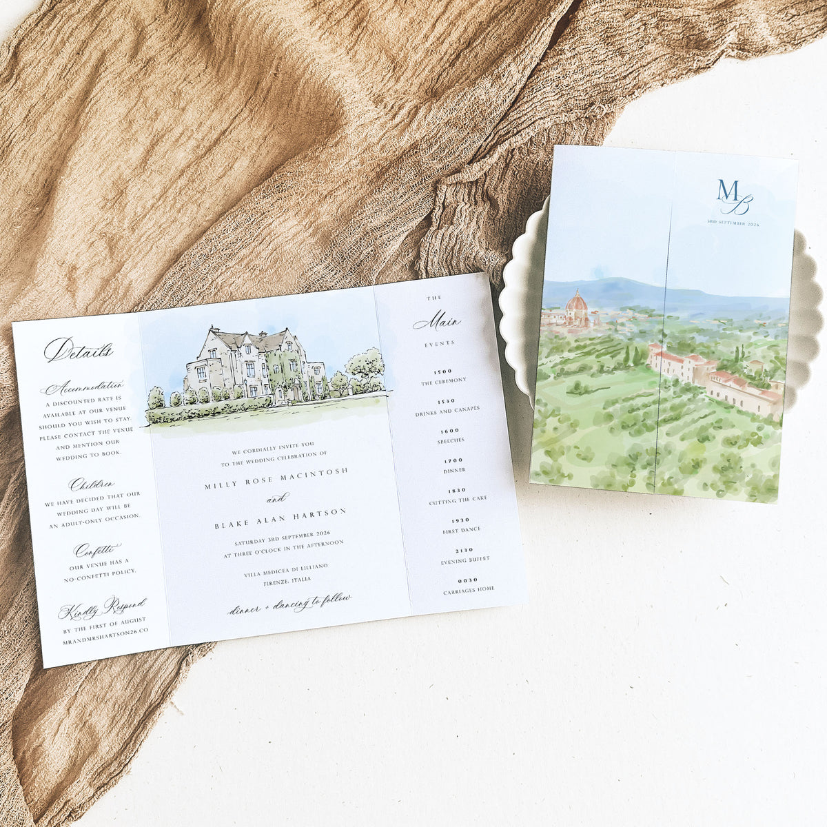 An illustrated gatefold wedding invitation showed open and closed with venue and landscape watercolour illustration and elegant text, styled on a rustic wood slice over a white surface.
