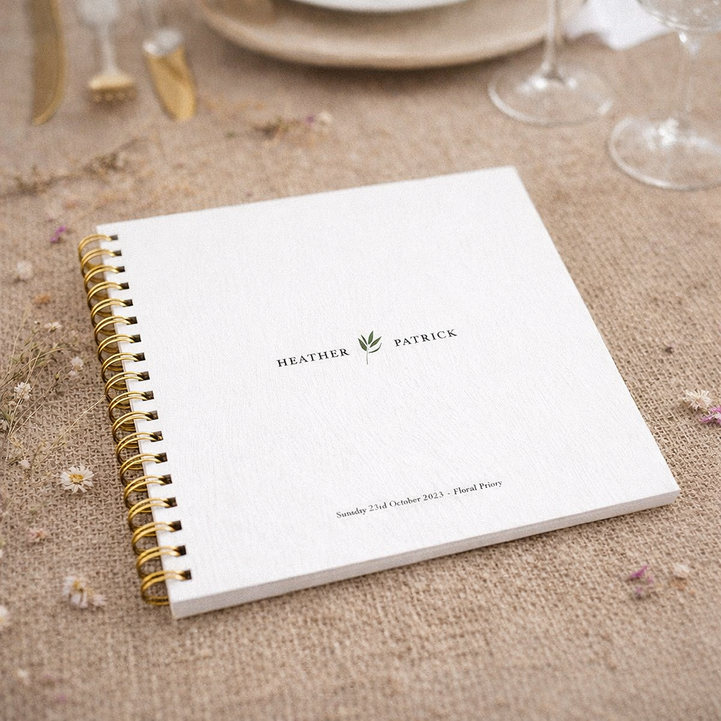 White guestbook with gold spiral binding on a textured surface