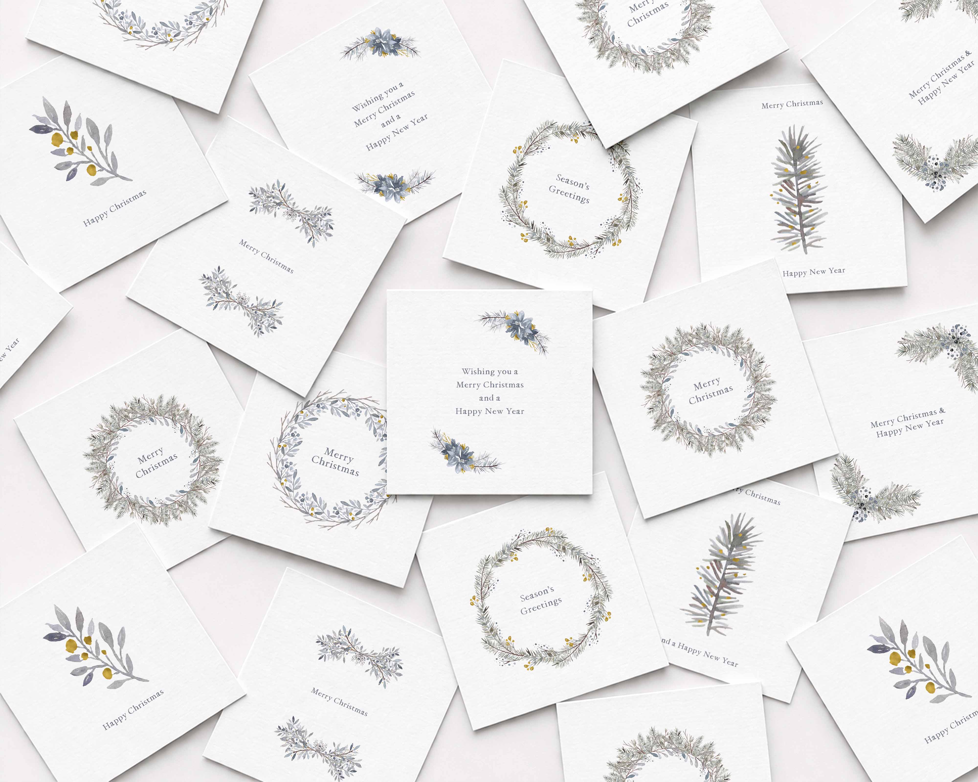 A scattered arrangement of white Christmas cards featuring delicate botanical illustrations in muted gray, blue, and yellow, including wreaths, sprigs, and small text such as Merry Christmas and Happy New Year.