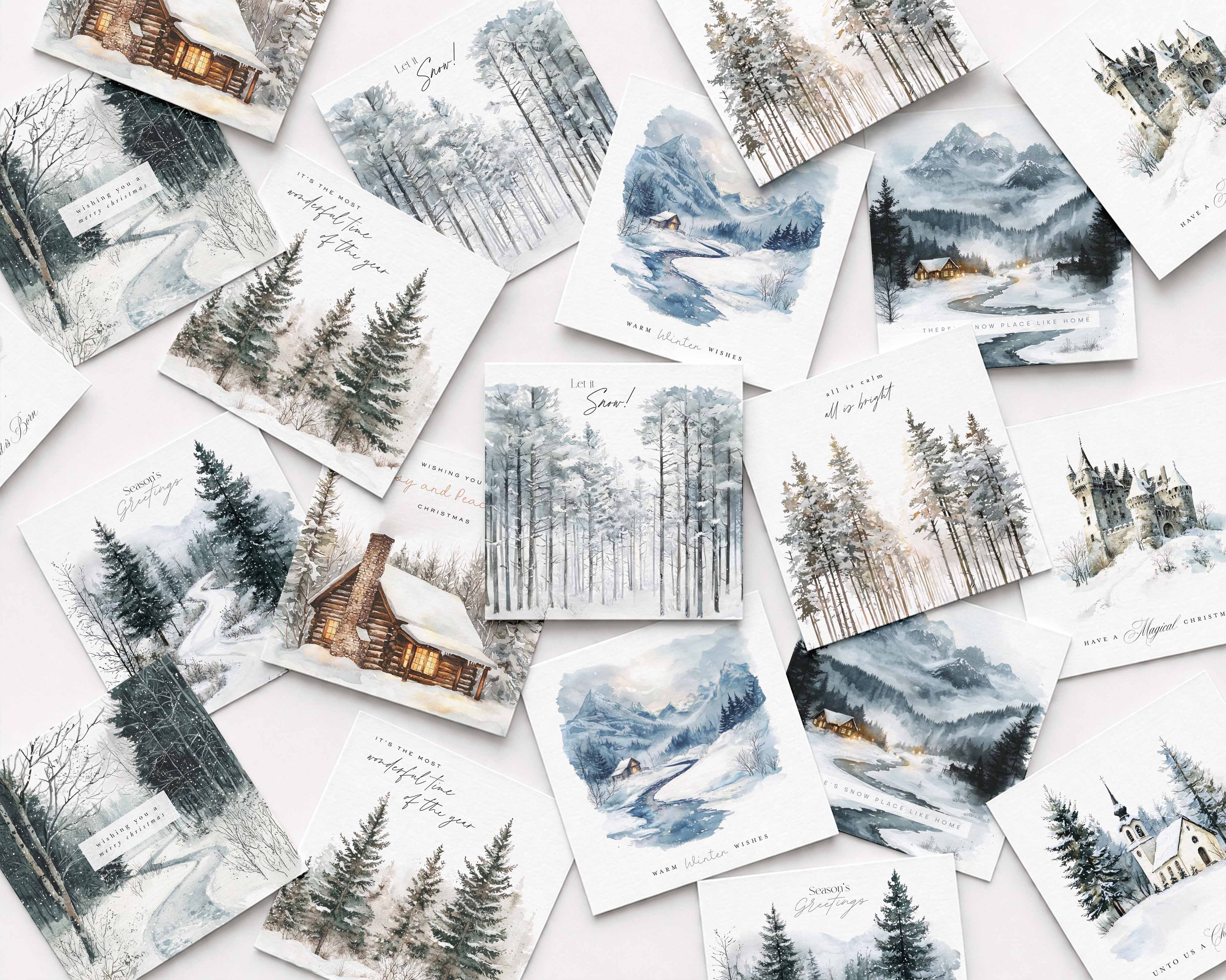 A flat-lay arrangement of multiple watercolor winter landscape Christmas cards scattered on a light background. The prints depict snowy forests, mountains, cabins, and rivers in soft blue, gray, white, and brown tones, with some cards featuring handwritten text and small holiday greetings.