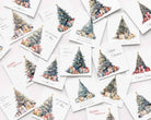A flat-lay arrangement of multiple white Christmas greeting cards scattered on a light background. Each card features a watercolor illustration of a decorated Christmas tree with wrapped presents, with holiday greetings such as 'Happy Christmas' and 'Merry Christmas' in elegant script.