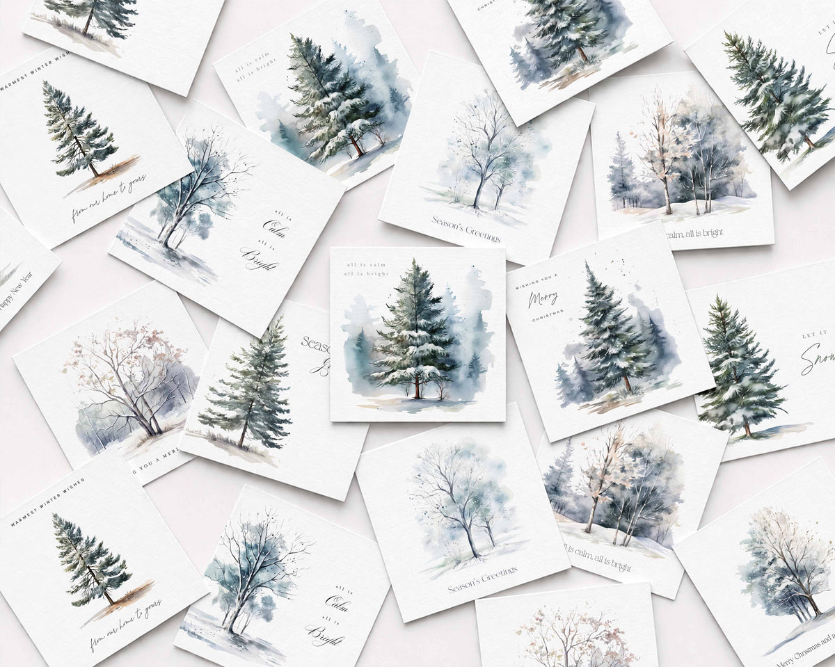 A flat-lay arrangement of multiple Christmas cards featuring watercolor winter trees and snowy forest scenes in soft blue, gray, and green tones on white backgrounds.