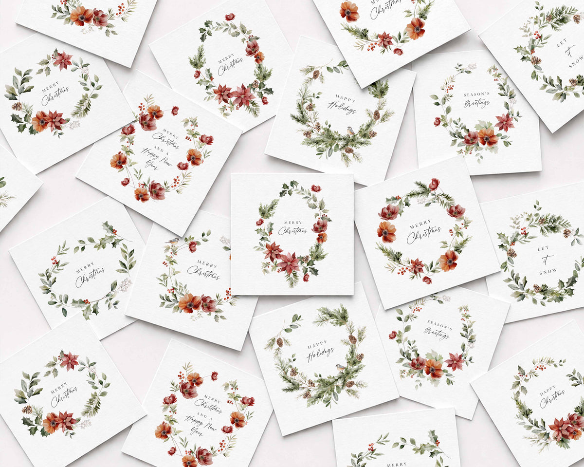 A flat-lay arrangement of multiple white square Christmas cards scattered on a light background, each printed with a watercolor floral wreath and holiday greeting text.