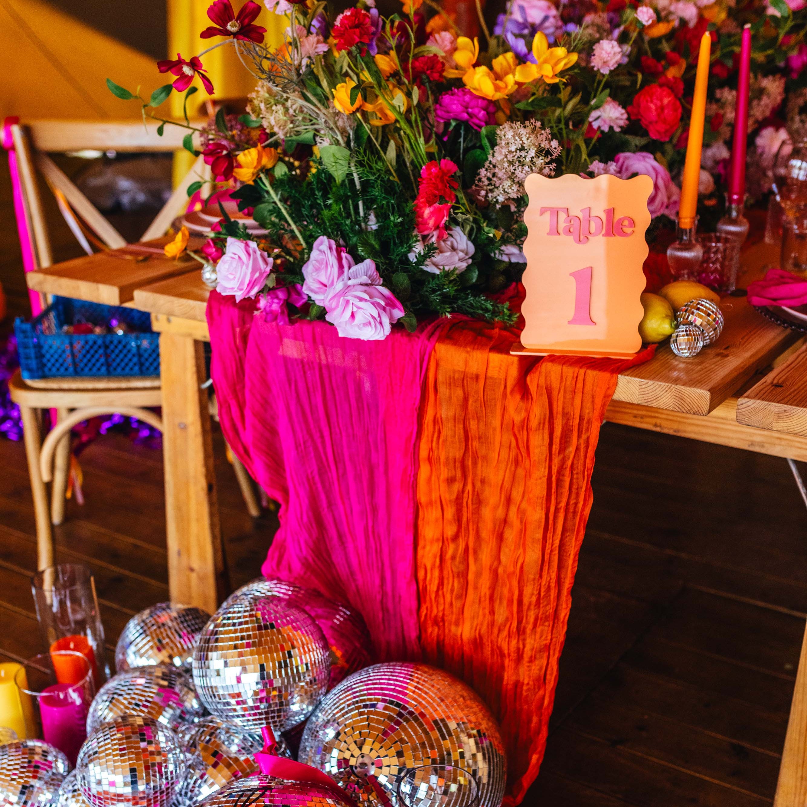 Decorative table setup with colorful flowers, disco balls, and a 'Table 1' sign on a wooden floor.