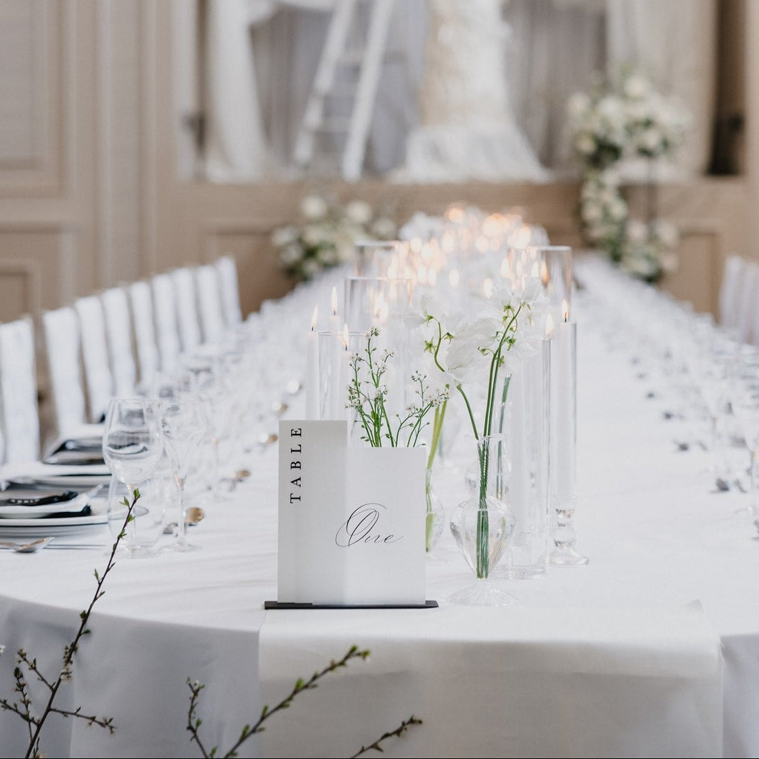 Elegant dining table setup in a formal event room with white tablecloth, chairs, and centerpieces.