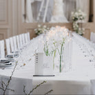 Elegant dining table setup in a formal event room with white tablecloth, chairs, and centerpieces.
