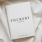 A hardcover book titled 'FUCKERY IS AFOOT' by David Cole, displayed on a soft, draped cream-colored fabric background.