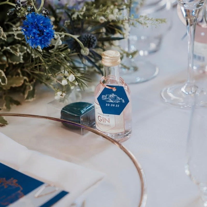 Miniature bottle of gin on a table with floral decorations and glasses.