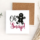 A square white snap card with a black gingerbread man illustration and the words 'Oh Snap!' in black and dark pink script, shown with a cork backing on a light wood surface.