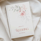 a5 white hardcover notebook with pink and green floral watercolour in the top right, and the phrase "amelias wedding notebook" in pink text at the bottom