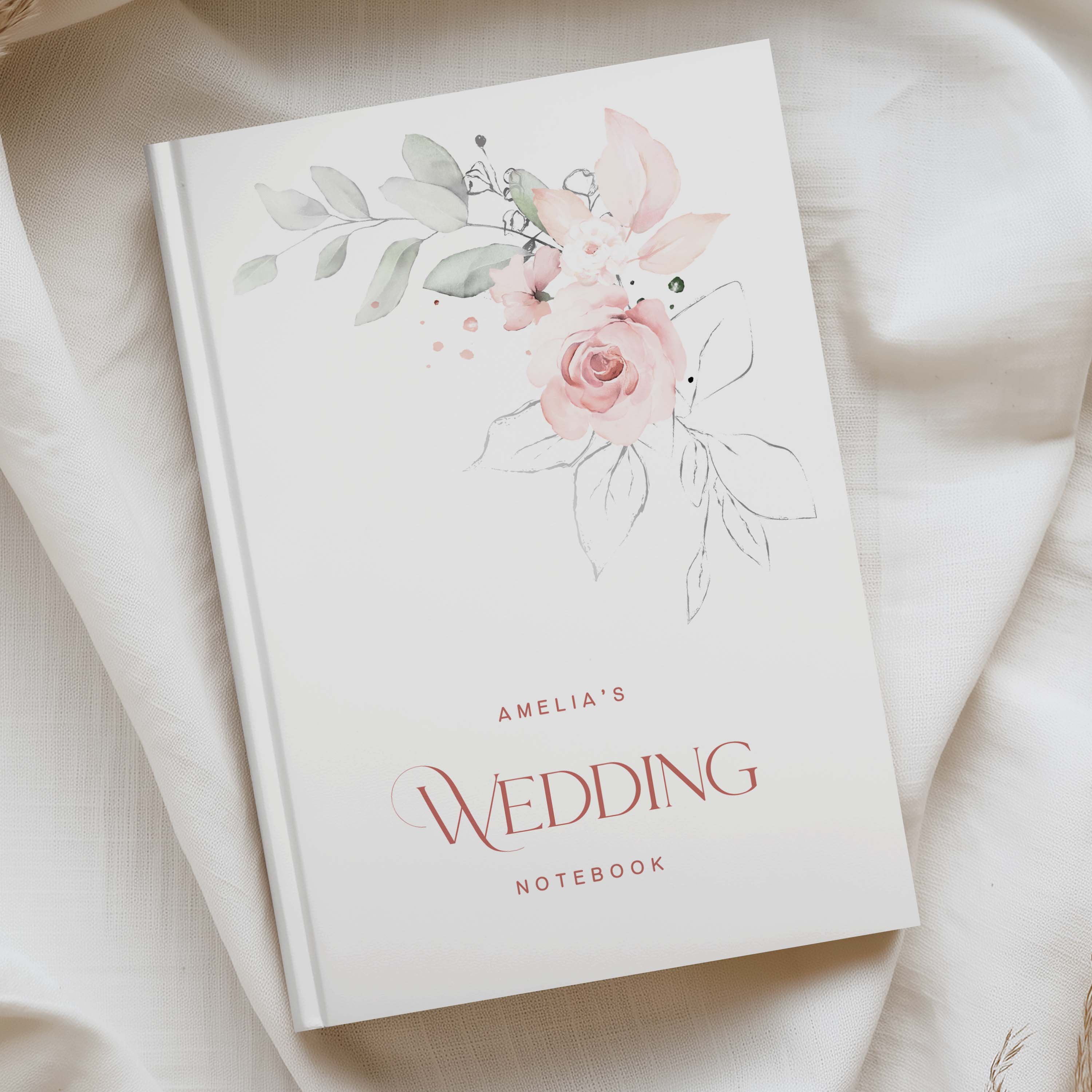 a5 white hardcover notebook with pink and green floral watercolour in the top right, and the phrase "amelias wedding notebook" in pink text at the bottom