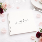 white wedding guest book with white binder on white table cloth with blush and burgundy petals and flowers