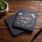 Slate with 'Happy Father's Day' text on a wooden surface with a pen and plant.