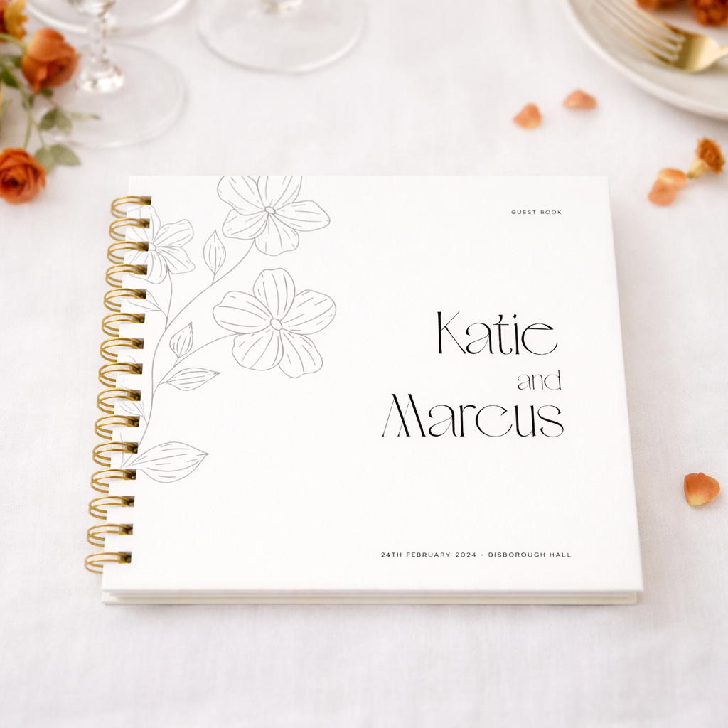 white guest book with gold binder with orange petals and flowers on white tablecloth