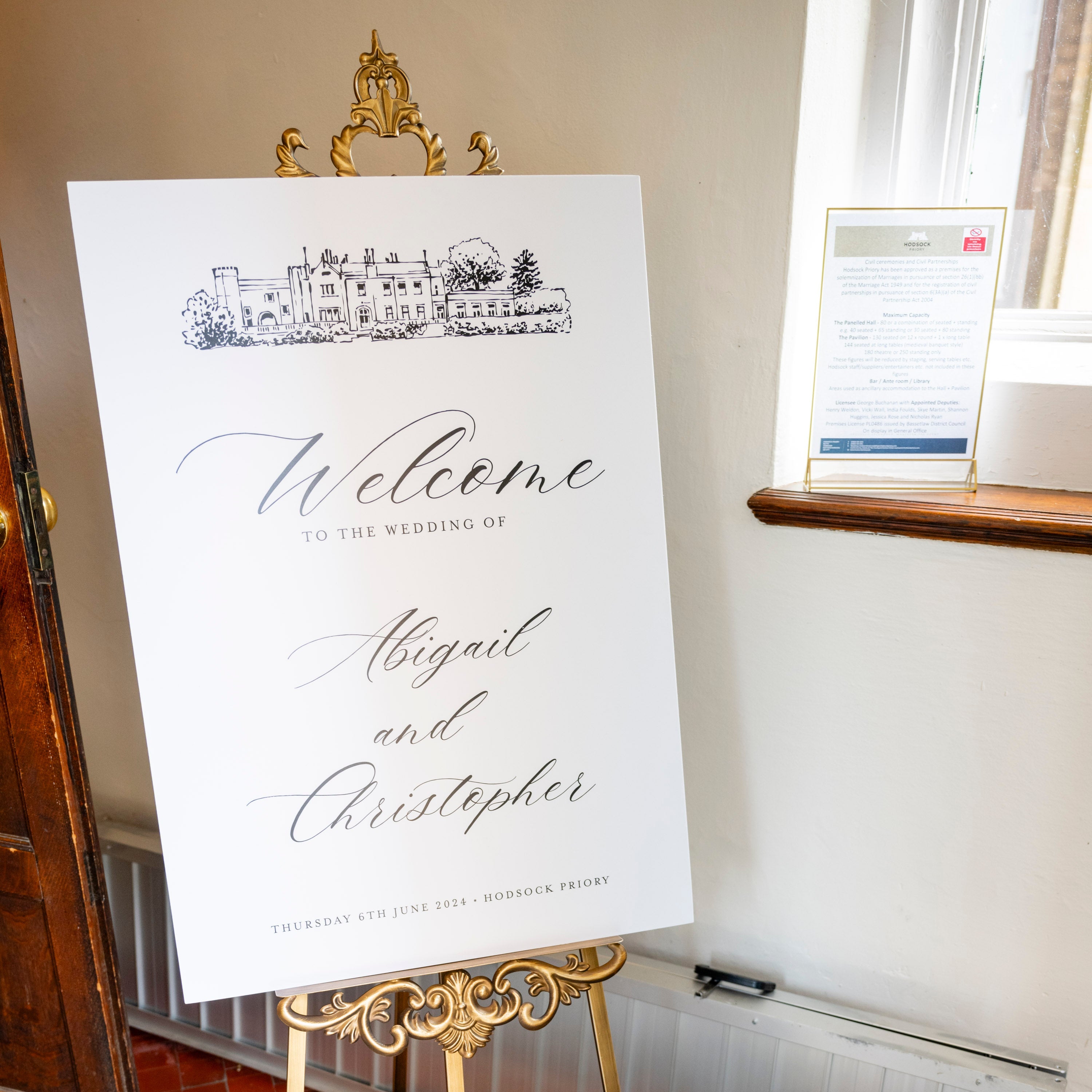 Decorative wedding welcome sign on a gold stand with candles and flowers in a room.